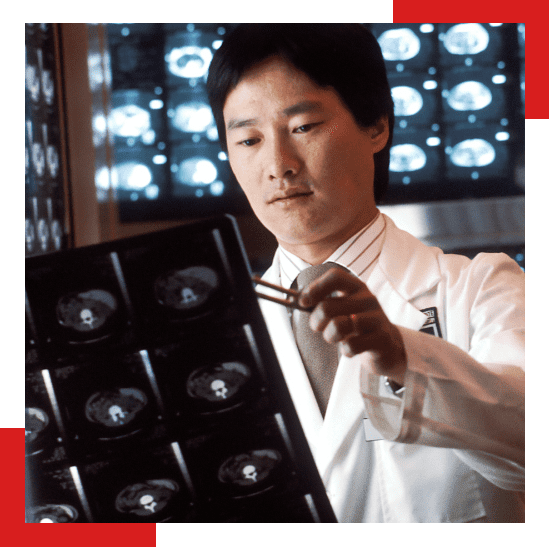 Doctor in a white lab coat examining a series of brain scan X-rays with a pen-like pointer, with illuminated medical imaging screens in the background.