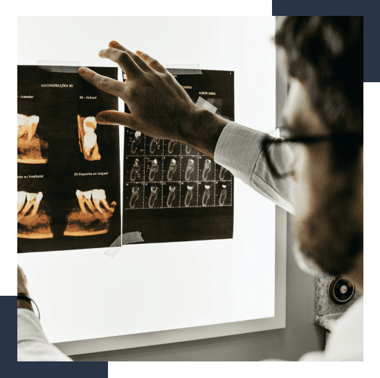Dentist or radiologist examining dental X-rays and 3D scan images of teeth and jawbone, held up against a backlit screen.