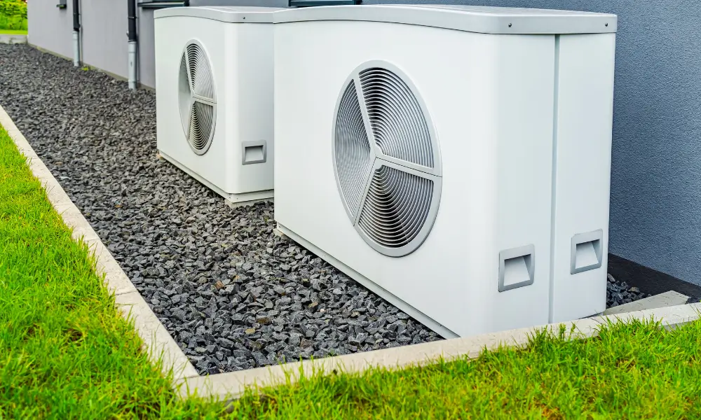 Two large white air to air heat pumps outside a property.