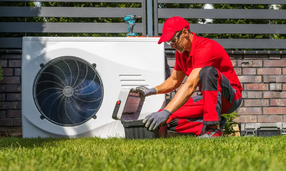 Eine Wärmepumpe in einem Garten wird von einem Techniker in roter Uniform mit Mütze gewartet.