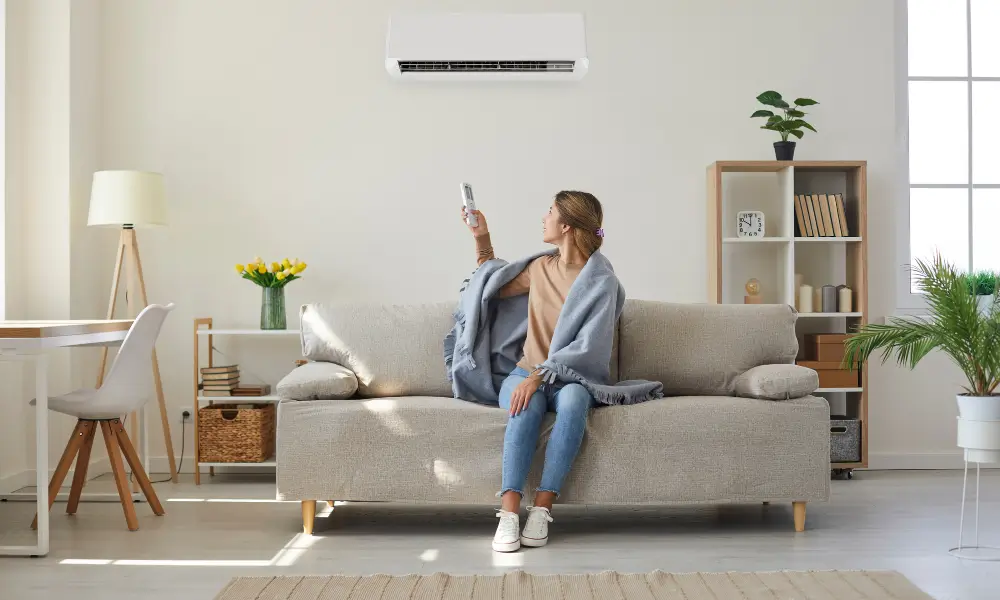 Woman sitting on her sofa, with a blanket controlling her HVAC system.