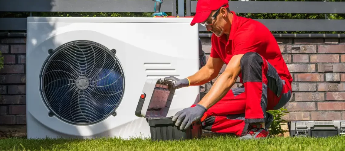 Eine Wärmepumpe in einem Garten wird von einem Techniker in roter Uniform mit Mütze gewartet.